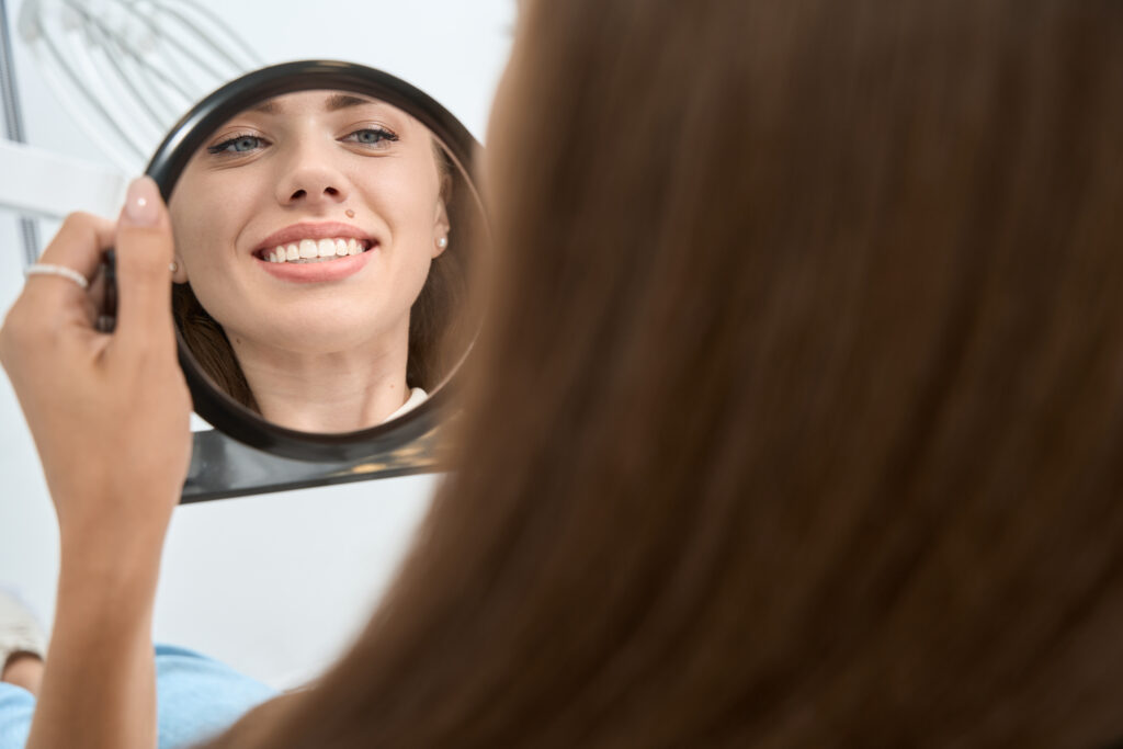 Woman admiring her restored smile in a mirror after cosmetic dentistry in Twin Falls at Green Acres Family Dentistry